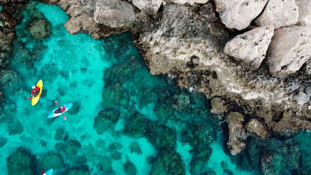 View of a drone from a drone people are kayaking in the sea near the mountains in a cave